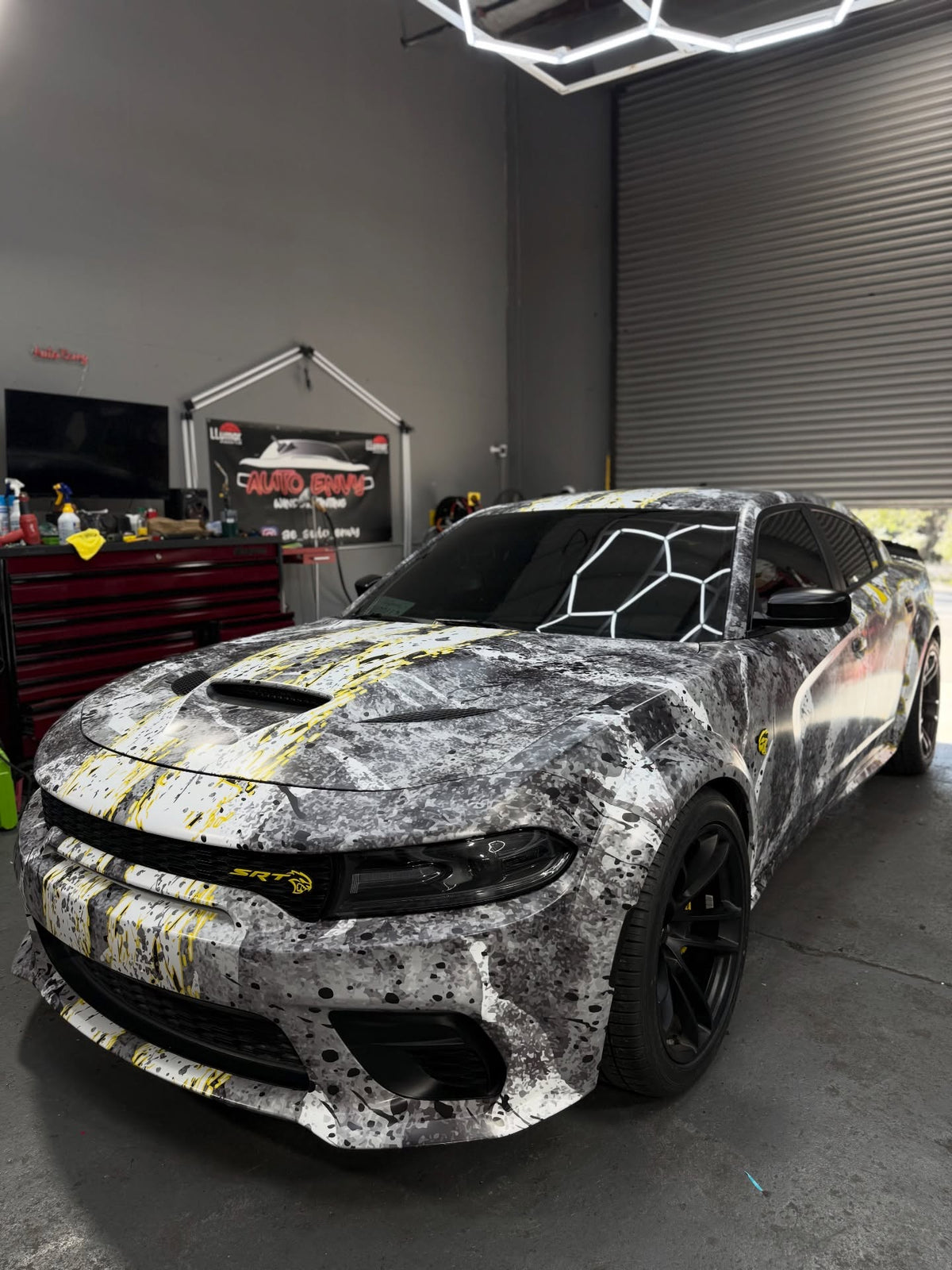 Grey and yellow splatter wrap on a widebody Dodge Charger in the install shop, designed by JCD