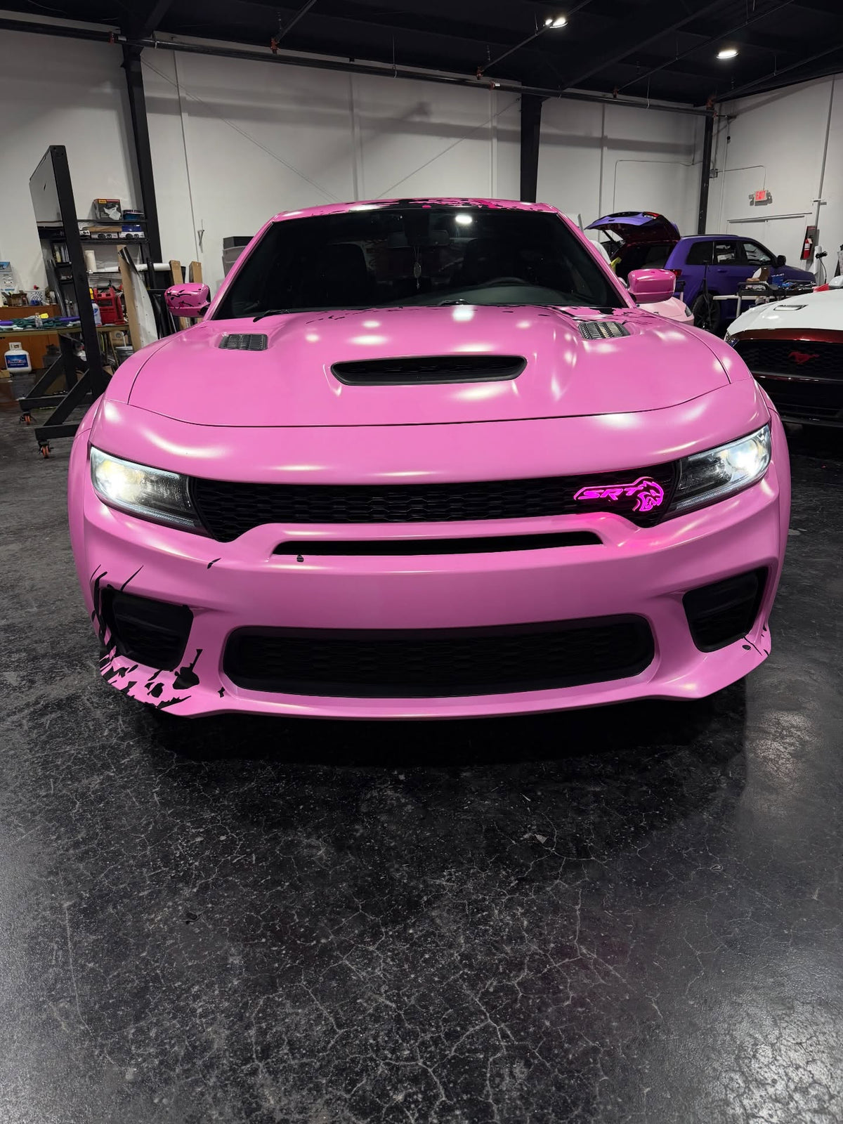 Front view of the pink wrapped Dodge Charger Hellcat with a glowing SRT grille badge, designed by JCD