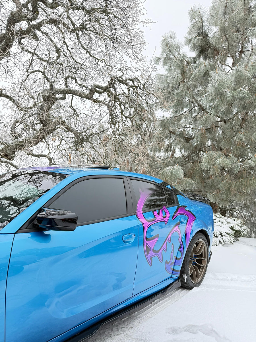 Side view of a custom chrome-fade Hellcat decal on a blue Dodge Charger in the snow, designed by JCD