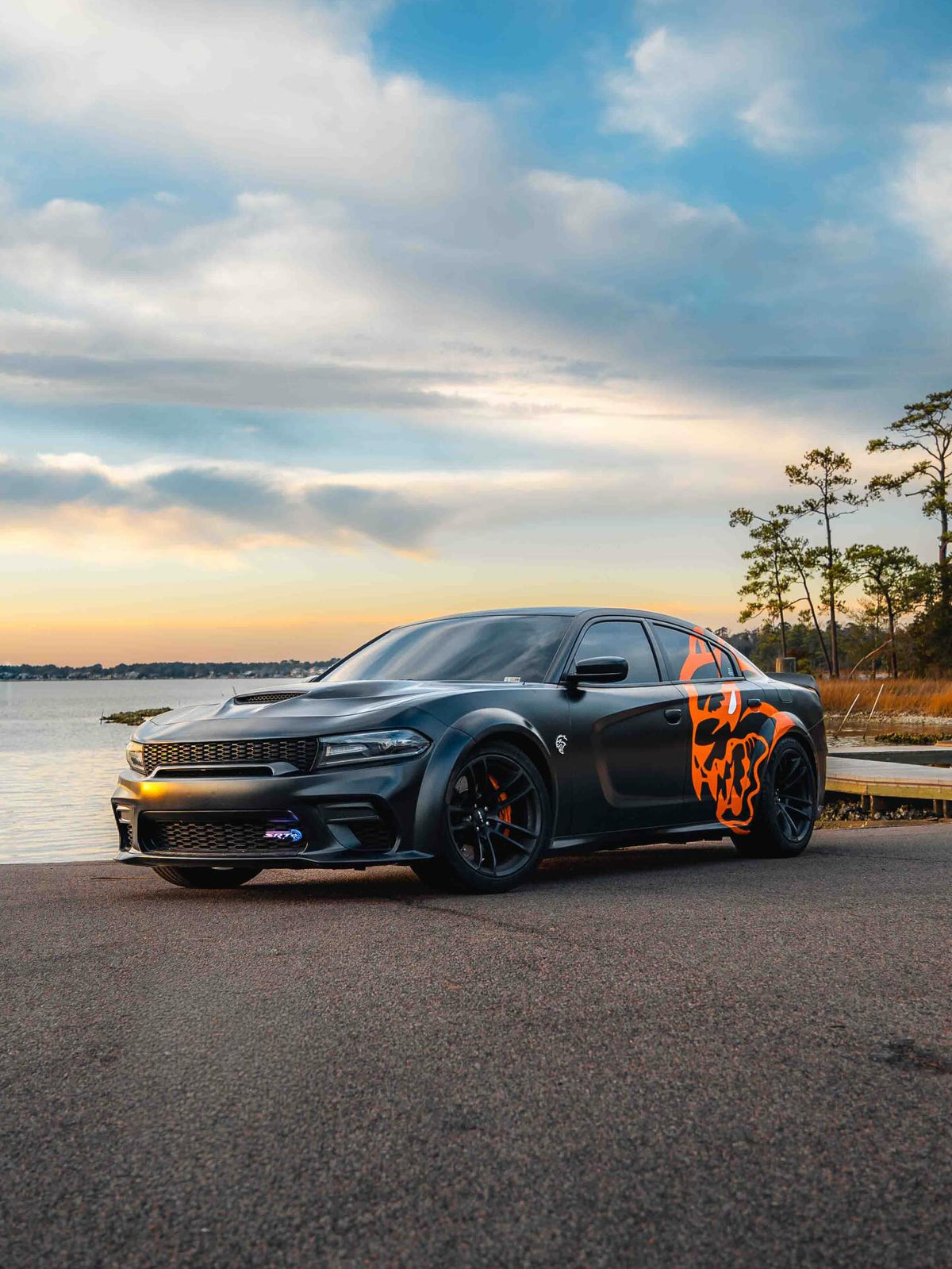 Orange custom side graphic decal on a satin black widebody Dodge Charger Hellcat at sunset, designed by JCD