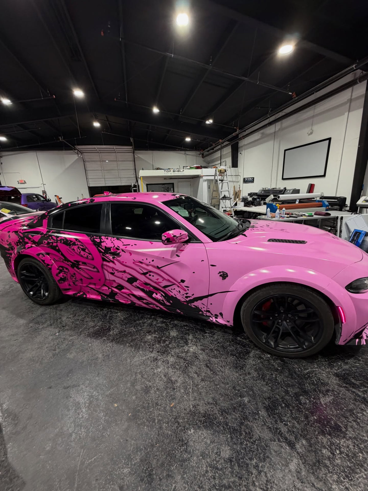 Side view of the two-tone pink abstract wrap on a Dodge Charger Hellcat in the install shop, designed by JCD